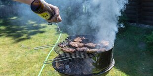 Bauchfleisch und Würstchen auf einem Grill werden mit Bier abgelöscht