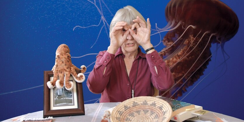 Donna Haraway blickt neben einer Krakenpuppe in die Ferne.