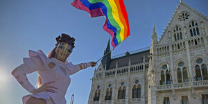 Eine Drag Queen mit einer Rgenbogenflagge vor dem ungarischen Parlament