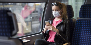 Frau mit Mundschutzmaske, sitzt in Zug, am Handy,