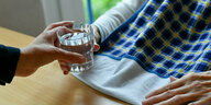 Eine Pflegerin reicht einer Seniorin ein Glas Wasser
