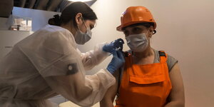 Eine Frau mit Schutzlhelm und oranger Arbeitskleidung bekommt eine Impfung