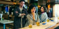 Zwei Frauen und ein Mann stehen an der Bar, vor ihnen ihre Bierkrüge