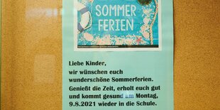 „Sommerferien“ und gute Wünsche für die Schülerinnen und Schüler stehen auf einem Papier im Glaskasten einer Grundschule in Prenzlauer Berg geschrieben