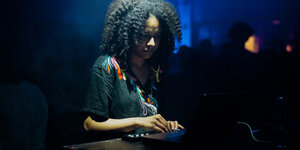 Die Elektromusikerin Jessica Ekomane steht auf der Bühne an einem Mischpult