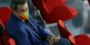 Markus Söder sitz auf den Rängen des EM-Stadions und trägt eine Mundschutzmaske in Regenbogenfarben