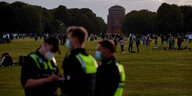 Polizisten stehen vor einer Wiese im Stadtpark, auf der Jugendliche feiern