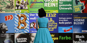 Frau im hellblauen Kleid steht vor bunter Plakatwand im Museum