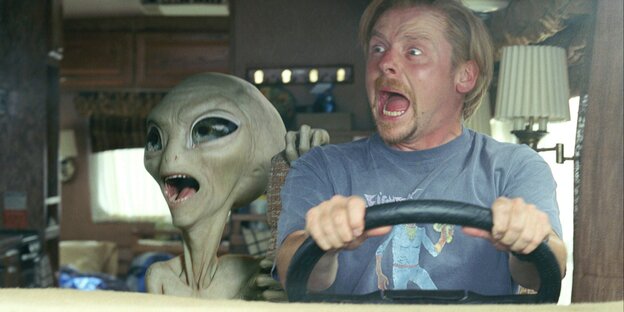 Der Alien Paul aus dem gleichnahmigen Film sitzt neben dem Schauspieler Simon Pegg im Auto. Beide schreien. Pegg umklammert das Lenkrad.