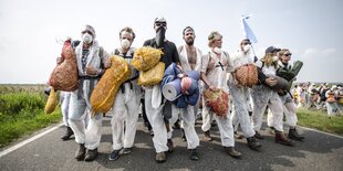 Eine gruppe von jungen Männer geht eng nebeneinander eine Straße entlang. Sie alle tragen weiße Overalls.