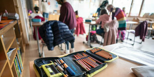 Ein Mäppchen liegt auf einer Schulbank, dahinter Kinder