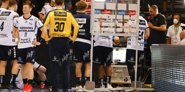 Handballspieler stehen vor einem Fernseh-Bildschirm