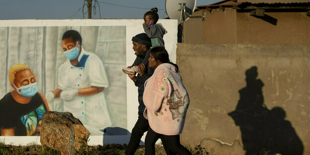 Eine Familie geht an einem Wandbild vorbei, das für eine Corona-Impfung wirbt