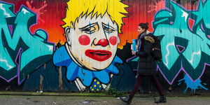 Eine Frau läuft an einem Graffiti vorbei, das Boris Johnson als Clown zeigt