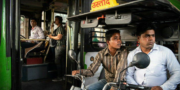 Watender Fahrer in einer Rikscha, im Hintergrund Bus mit offener Tür.