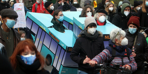 Aktivisten stecken während einer Demonstration in Bussen aus Pappe, um einen kostenlosen ÖPNV zu fordern - alle Demo-TeinehmerInnen tragen Mund-Nasenschutz