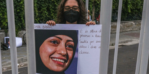 Eine Demonstrantion mit Mundschutz hält ein Plakat mit einem Foto der Aktivistin Samar Badawi