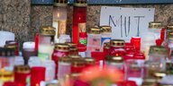 Ein Zettel mit der Aufschrift ·Mut· und "Angst" liegt inmitten von Trauerkerzen vor einem Kaufhaus in der Innenstadt