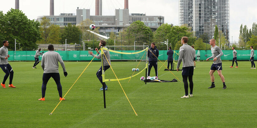 Mehrere MÄnne spielen Fußballtennis, im Hintergrund sind Wolfsburger Fabrikanlagen zu sehen.