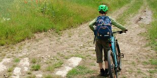 Ein Kind mit Fahrrad auf einer ungeteerten Feldstrasse