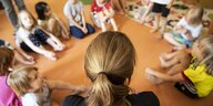 Erzieherin sitzt mit Kindern im Kindergarten im Kreis auf dem Boden
