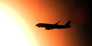 Ein Flugzeug fliegt an der untergehenden Sonne vorbei