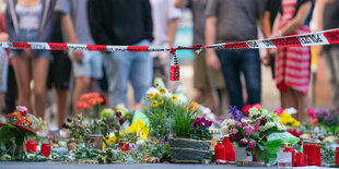 Trauerkerzen und Blumen liegen vor einem Kaufhaus in der Innenstad Würzburgs - dahinter stehen Menschen