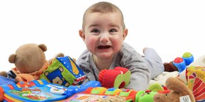 Ein weinendes Kleinkind liegt inmitten von Spielzeug auf einer Stoffdecke