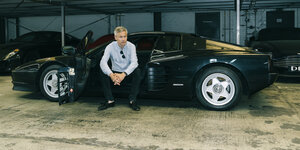 Ulf Poschardt sititz bei offener Farhertüre in einem Parkhaus im schwarzen Ferrari