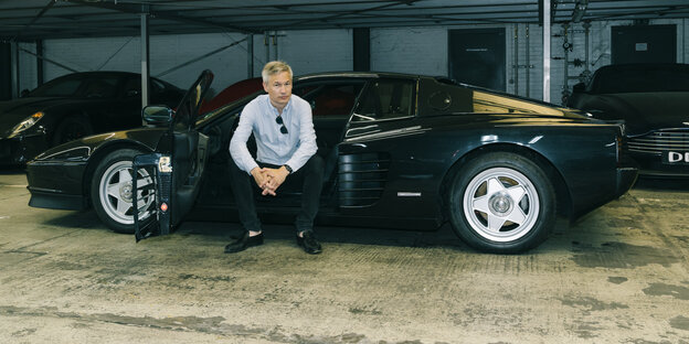 Ulf Poschardt sititz bei offener Farhertüre in einem Parkhaus im schwarzen Ferrari