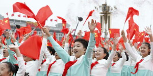Kinder in hellblauen Uniformen tragen rote Halsbänder, jubeln und schwenken chinesische Fahnen