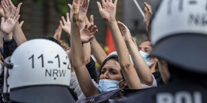 Demonstrierende mit Mund-Nasenschutz strecken ihre Hände in die Höhe-im Vordergrung Polizisten mit Helmen