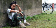 Eine junge Frau sitzt auf der Wiese, den Rücken gegen eine Mauer gestützt