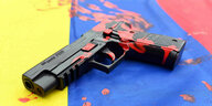 Auf einer kolumbianischen Fahne liegt eine untauglich gemachte Softairwaffe auf der Sig Sauer P226 steht und die mit roter Farbe bekleckert ist