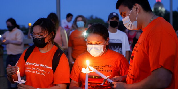 Mehrere Menschen in orangefarbnen T-Shirts entzünden Kerzen