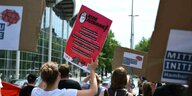 Junge Menschen halten bei einem Protest Schilder mit Forderungen für eine faire Beschäftigung in die Höhe