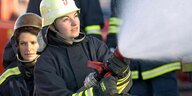 Eine Feuerwehrfrau im Einsatz hält einen Schlauch, aus dem unter hohem Druck Wasser spritzt
