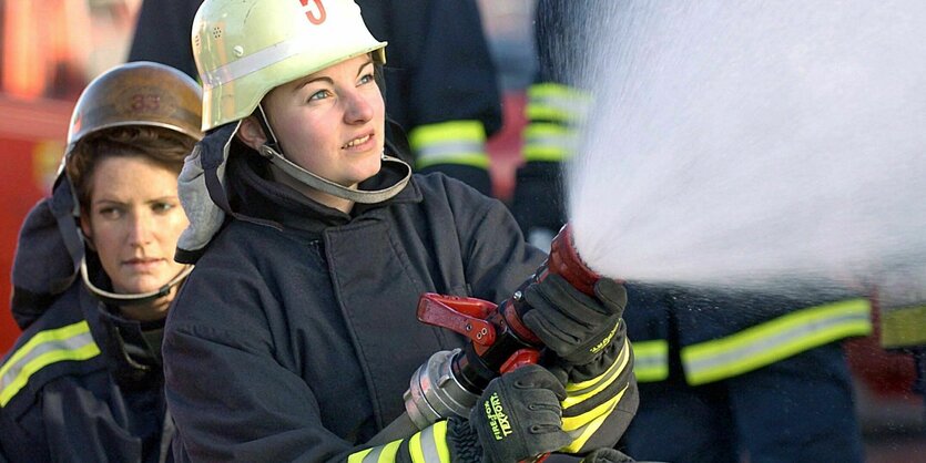 Eine Feuerwehrfrau im Einsatz hält einen Schlauch, aus dem unter hohem Druck Wasser spritzt