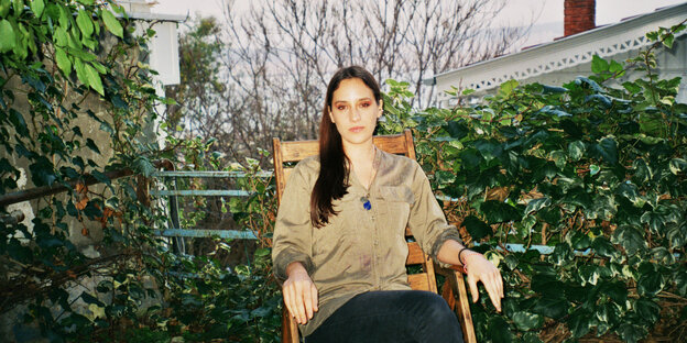 Filmemacherin Deniz Okyay sitzt in einem grünen Hinterhof auf einem Gartenstuhl