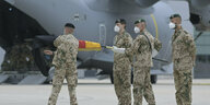Vier Bundeswehrsoldaten vor abgflugbereiter Maschine rollen deutsche Fahne zusammen