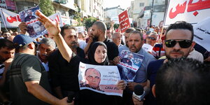 eine protestierende Menschenmenge, im Zentrum eine Frau mit Kopftuch und erhobenem Arm, in ihrer Hand ein Bild eines Mannes
