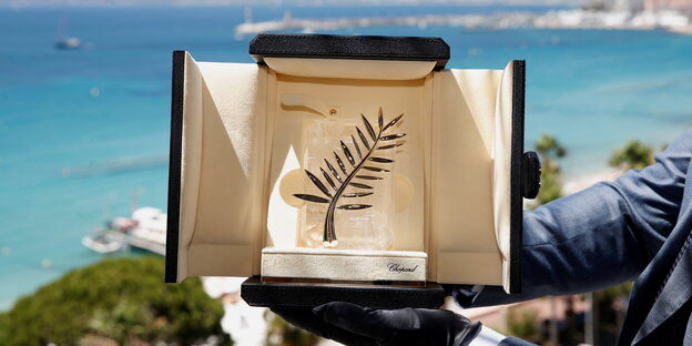 Präsentation des Hauptpreises der diesjährigen Filmfestspielen von Cannes: ein goldener Palmwedel in einer Schatulle wird von einer Person gehalten - im Hintergrund das Meer