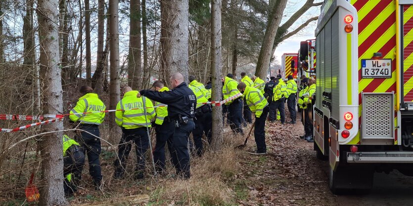 Polizeibeamte mit Einsatzfahrzeugen und Schaufeln an einem Waldrand