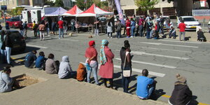 Menschen warten an einer Straße vor Zelten einer Covid-Teststation