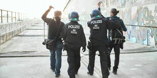 2 Fotojournalisten, die ihre Presseausweise in die Höhe halten, werden auf der Autobahnbaustelle von 2 Polizisten abgeführt