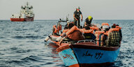 Kleines Boot mit geretteten Menschen in orangen Rettungswesten - im Hintergrund die Ocean Viking