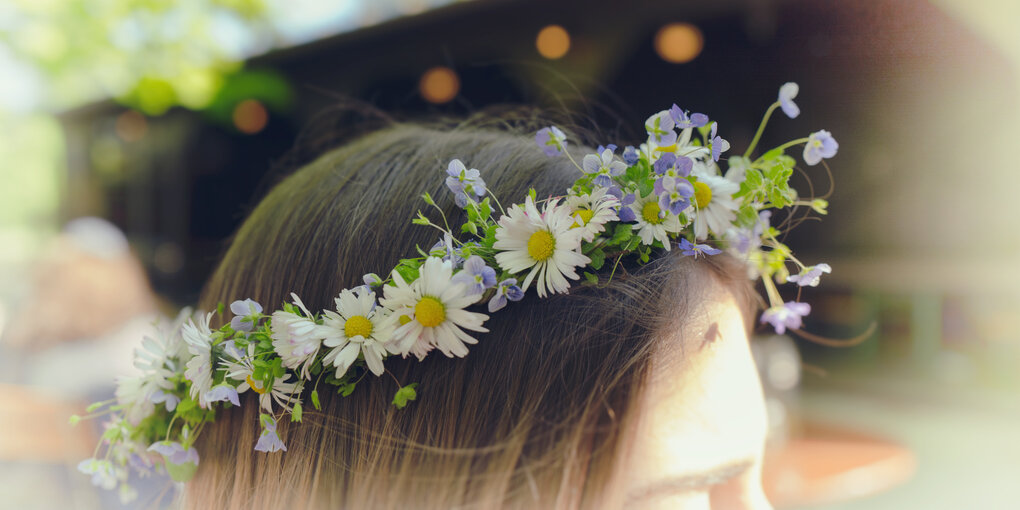 Blumenkette aus Gänseblümchen und blauen Blumen im Haar