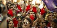 Demonstranten tragen während einer Demo rote Handschuhe und heben diese in die Höhe
