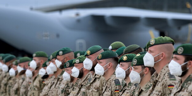 Soldaten stehem vor einem Bundeswehrflugzeug in einer Reihe und tragen Mund-Nasenschutz