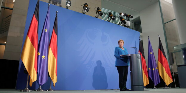 Angela Merkel spricht an einem Podeum vor blauem Hintergrund- neben ihr Deutschlandflaggen und Europaflaggen